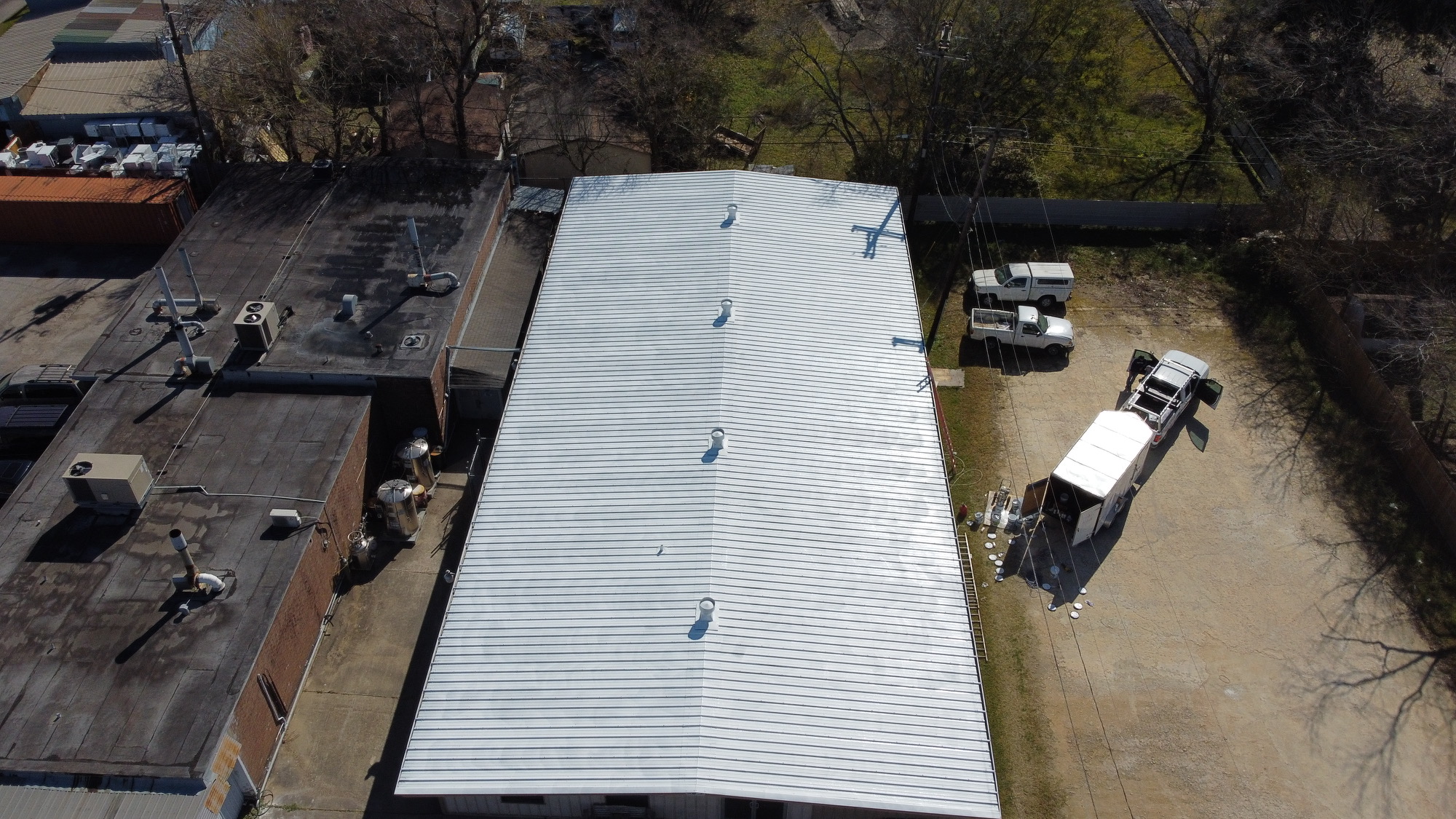 Coating crew equipment staged beside a commercial metal roof mid-restoration