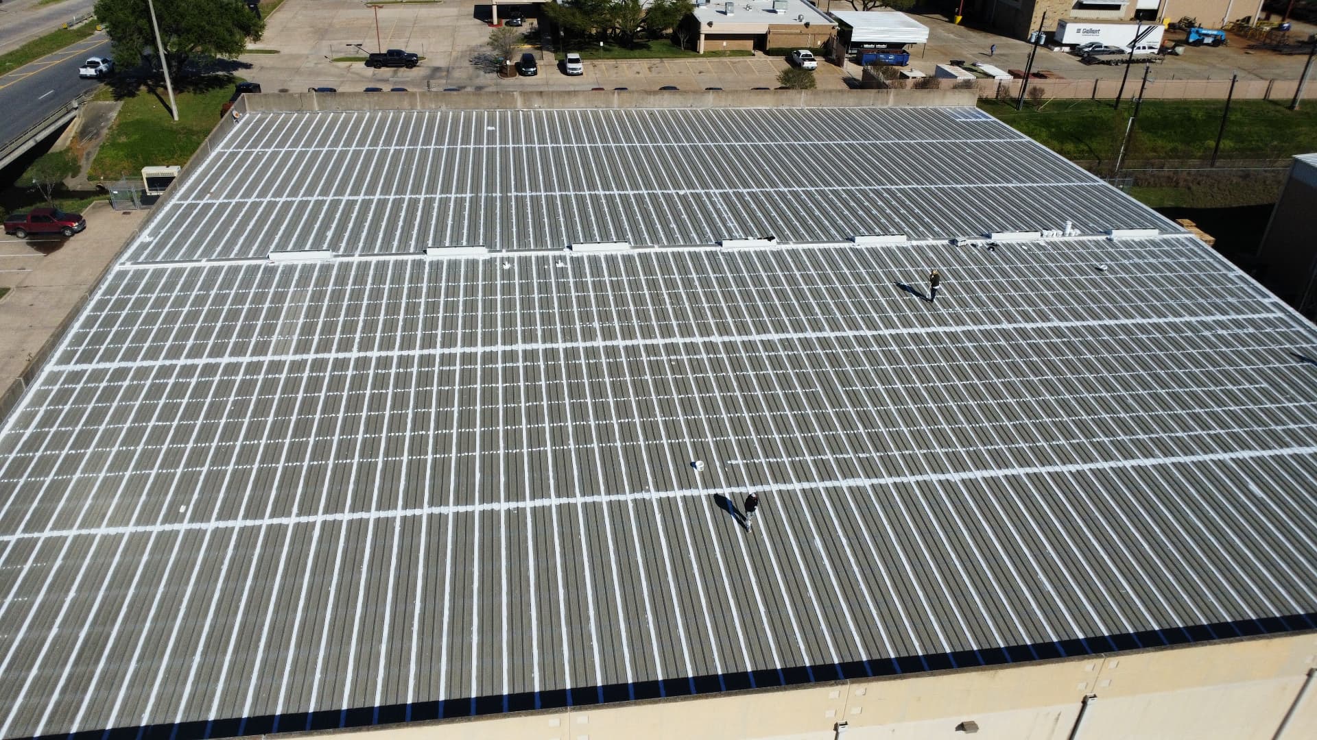 Aerial view of a commercial metal roof with white sealant applied along panel seams during scheduled maintenance